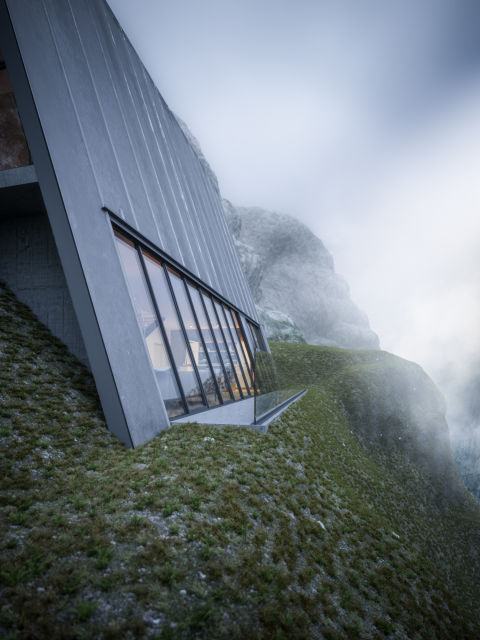 Разположена на ръба на стръмна скала, къщата е заградена от четири стъклени панела, които осигуряват постоянна естествена светлина и позволява на обитателите да се насладят на гледката към планината.